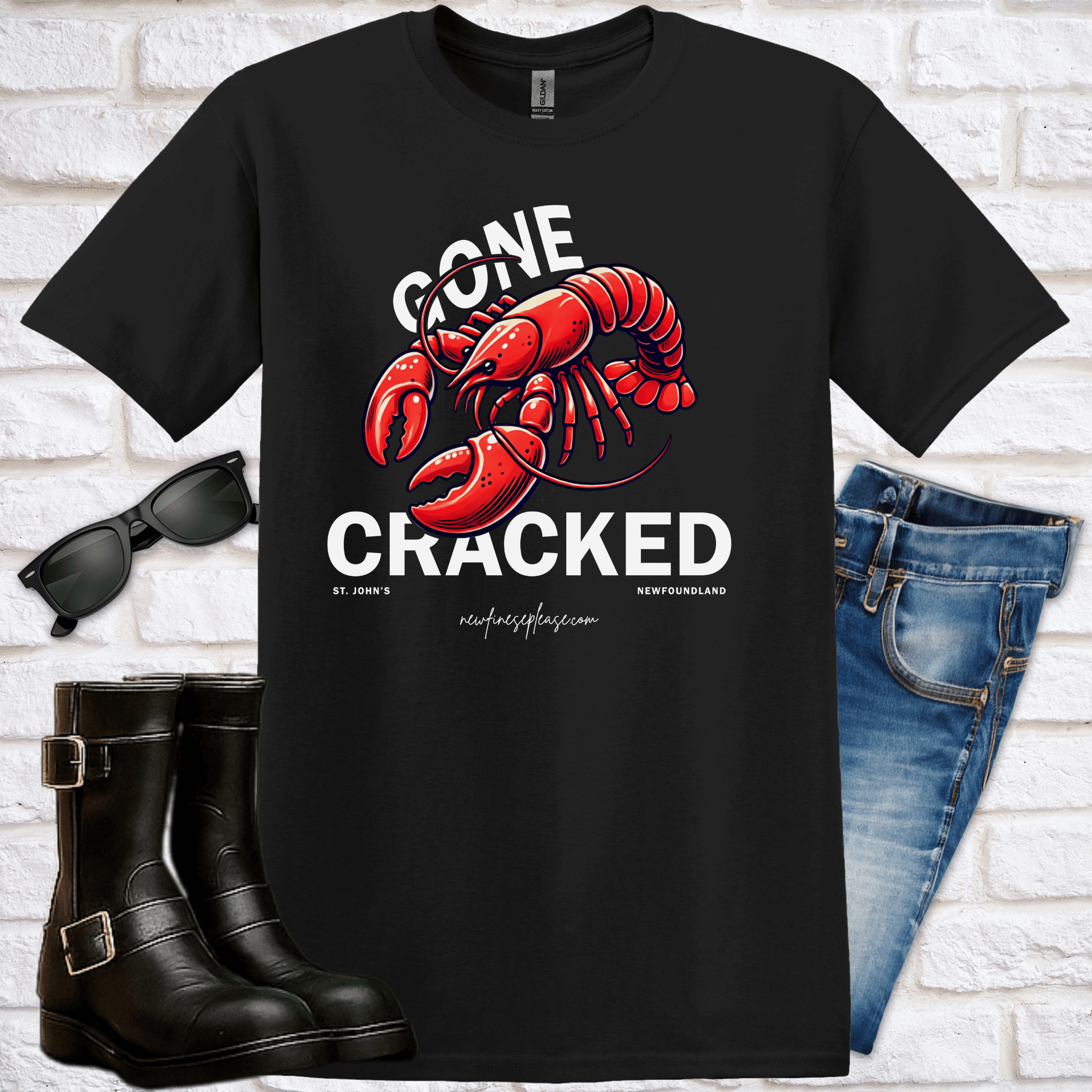 Flat-lay black t-shirt mockup with red lobster graphic and the words "Gone Cracked" with sunglasses, boots, and jeans on a white brick background