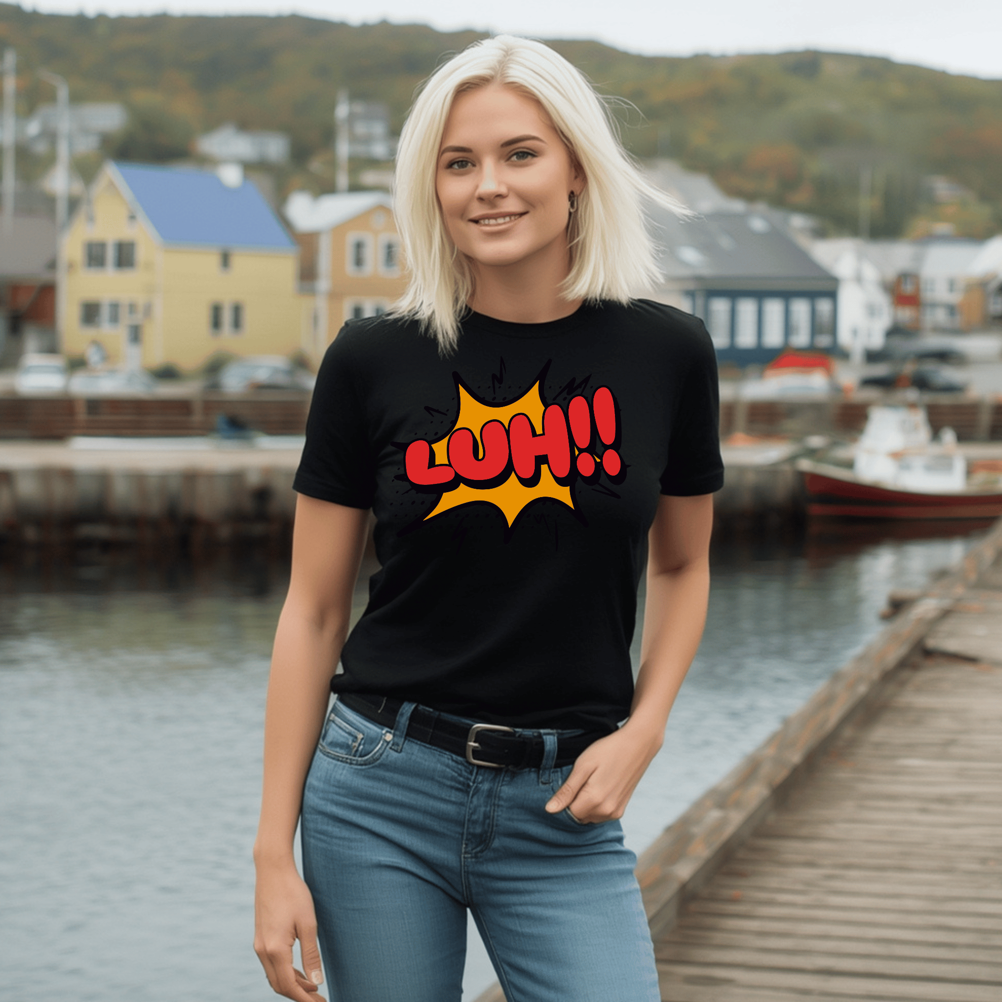Woman wearing a black t-shirt with 'Luh!!' comic design by a waterfront with houses and boats in the background.