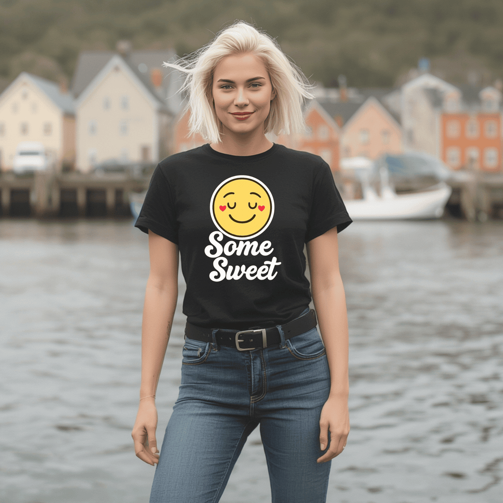 Woman wearing a black t-shirt with a smiley face emoji and text saying "Some Sweet" standing by a waterfront.