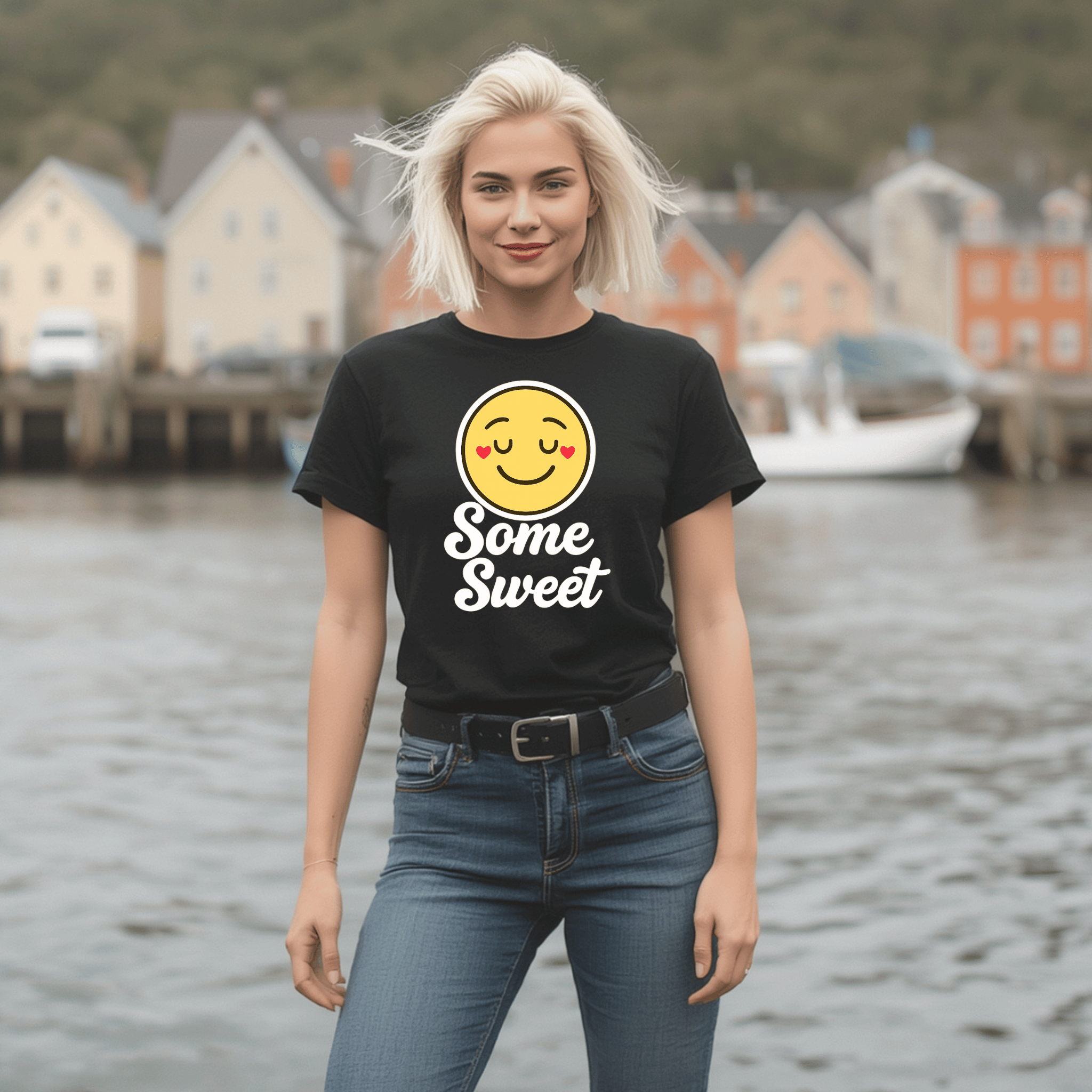 Woman wearing a black t-shirt with a smiley face emoji and text saying "Some Sweet" standing by a waterfront.