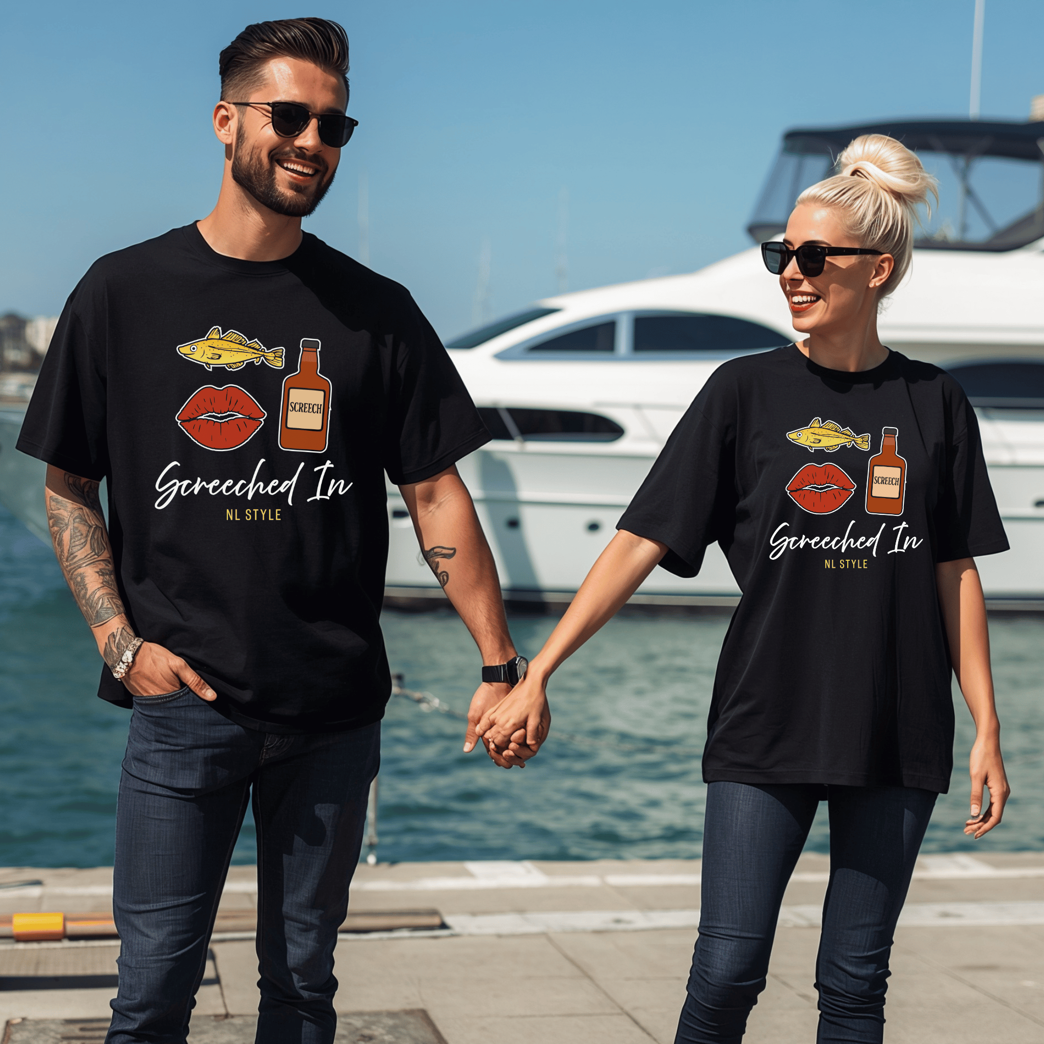 Two people wearing matching black t-shirts with graphic designs of a cod, a mouth and a bottle of screech and text saying "Screeched In--NL Style" standing by a waterfront.
