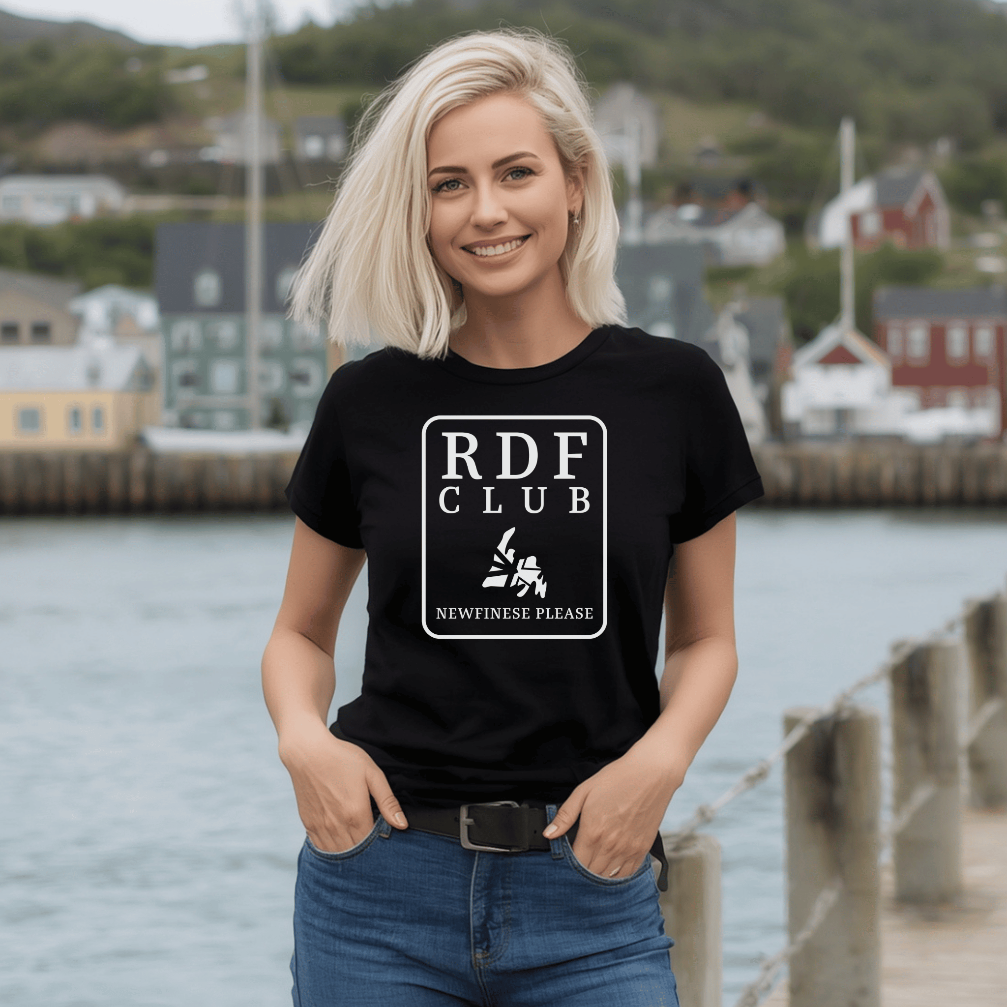 Woman wearing a black t-shirt with 'RDF Club' , a map of Newfoundland, and the Newfinese Please logo design by a waterfront.