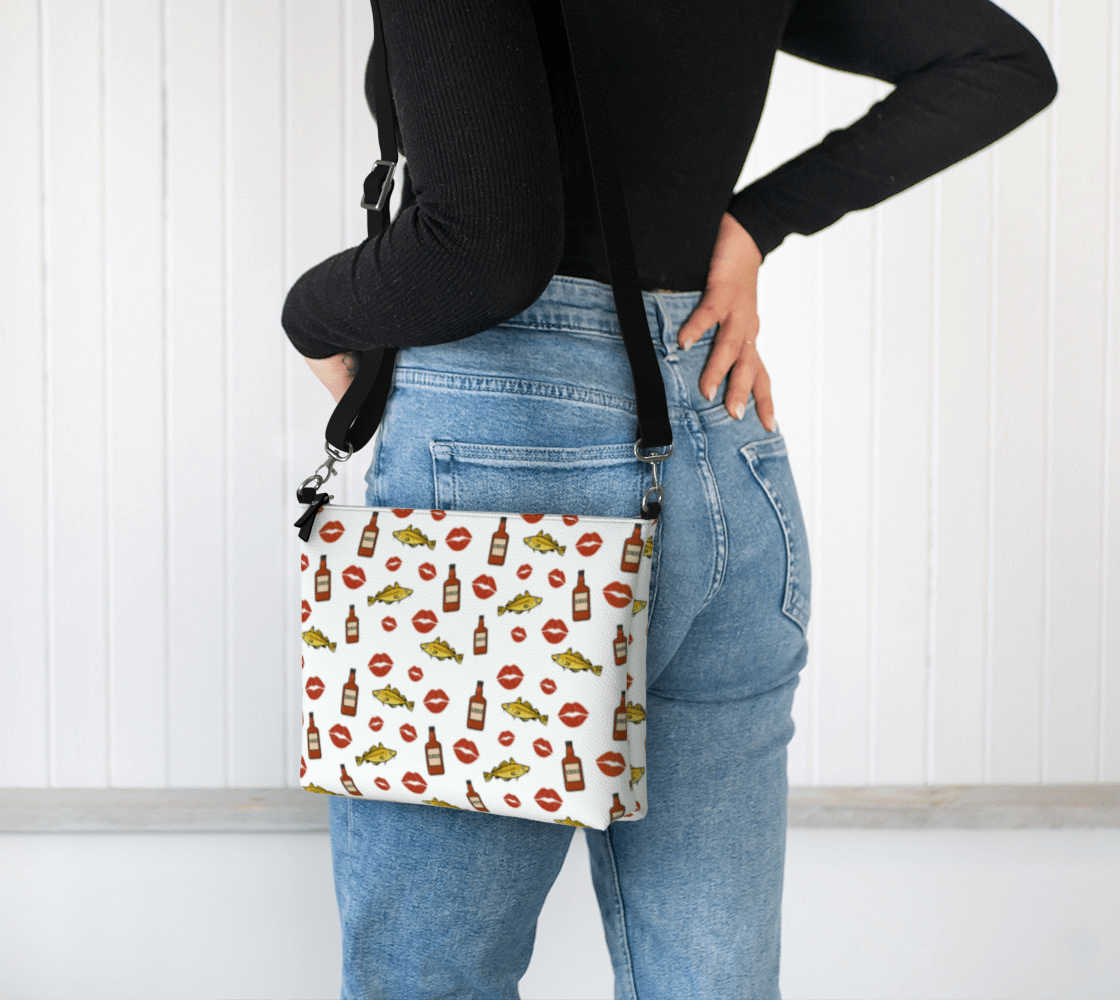 A model wearing a "Screeched In" Crossbody Purse,  featuring a fun pattern of codfish, lipstick kisses, and Screech rum bottles inspired by the iconic island tradition.