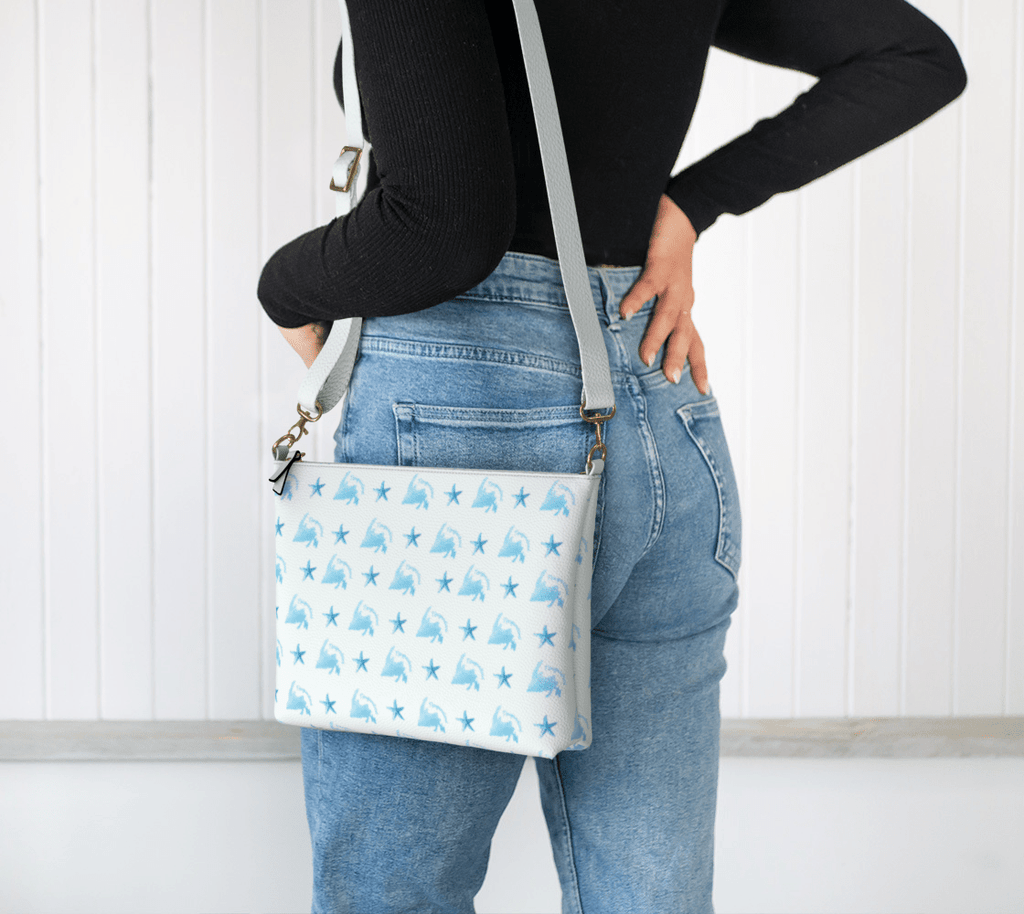 Woman wearing our Starfish Shores Crossbody Purse which features a soft blue pattern of starfish and Newfoundland outlines in flowing script.