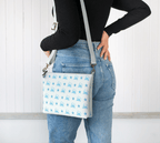 Woman wearing our Starfish Shores Crossbody Purse which features a soft blue pattern of starfish and Newfoundland outlines in flowing script.
