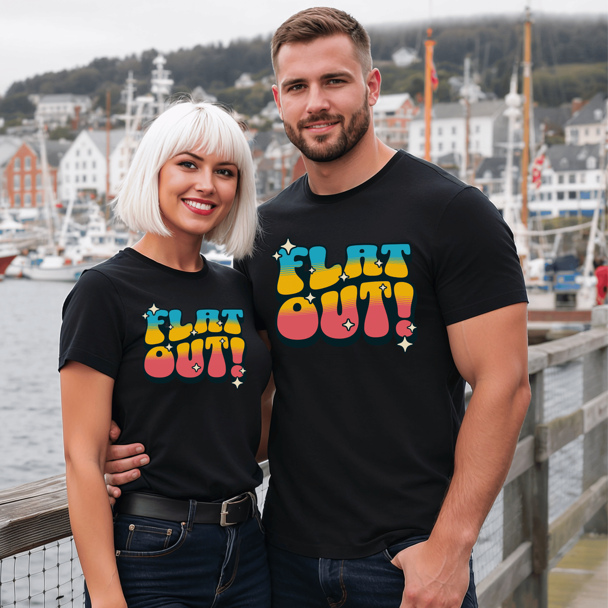 Two attractive people wearing black t-shirts with a retro-style 'FLAT OUT!' design by a waterfront.