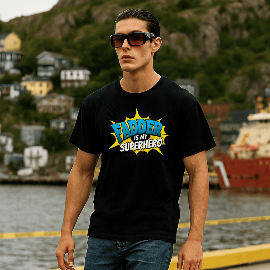 Man wearing a black t-shirt with 'FATHER IS MY SUPERHERO' text, standing by a waterfront with houses and a boat in the background.