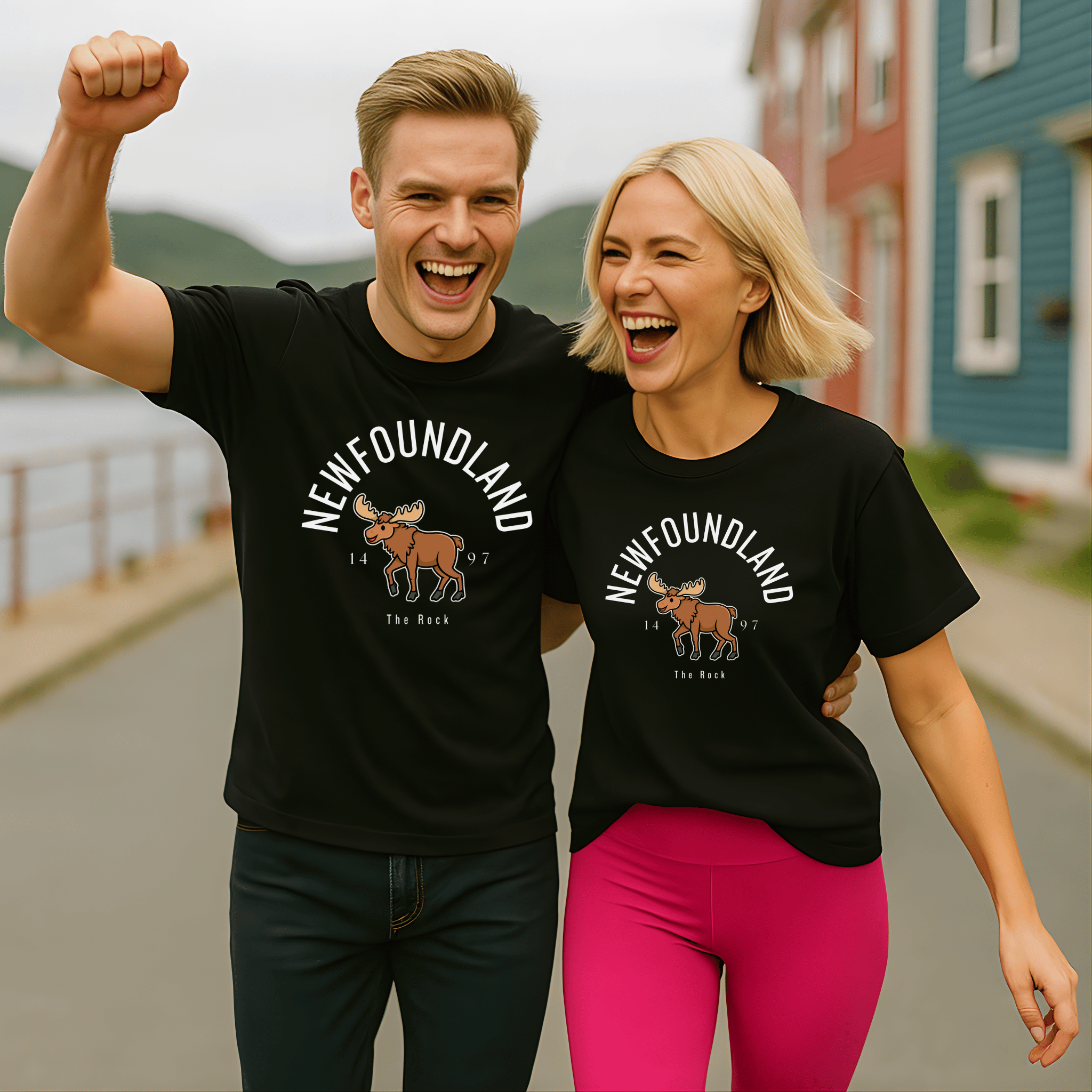 An attractive couple wearing matching black t-shirts with a moose graphic and 'Newfoundland', "1497," "The Rock" text, standing outdoors.