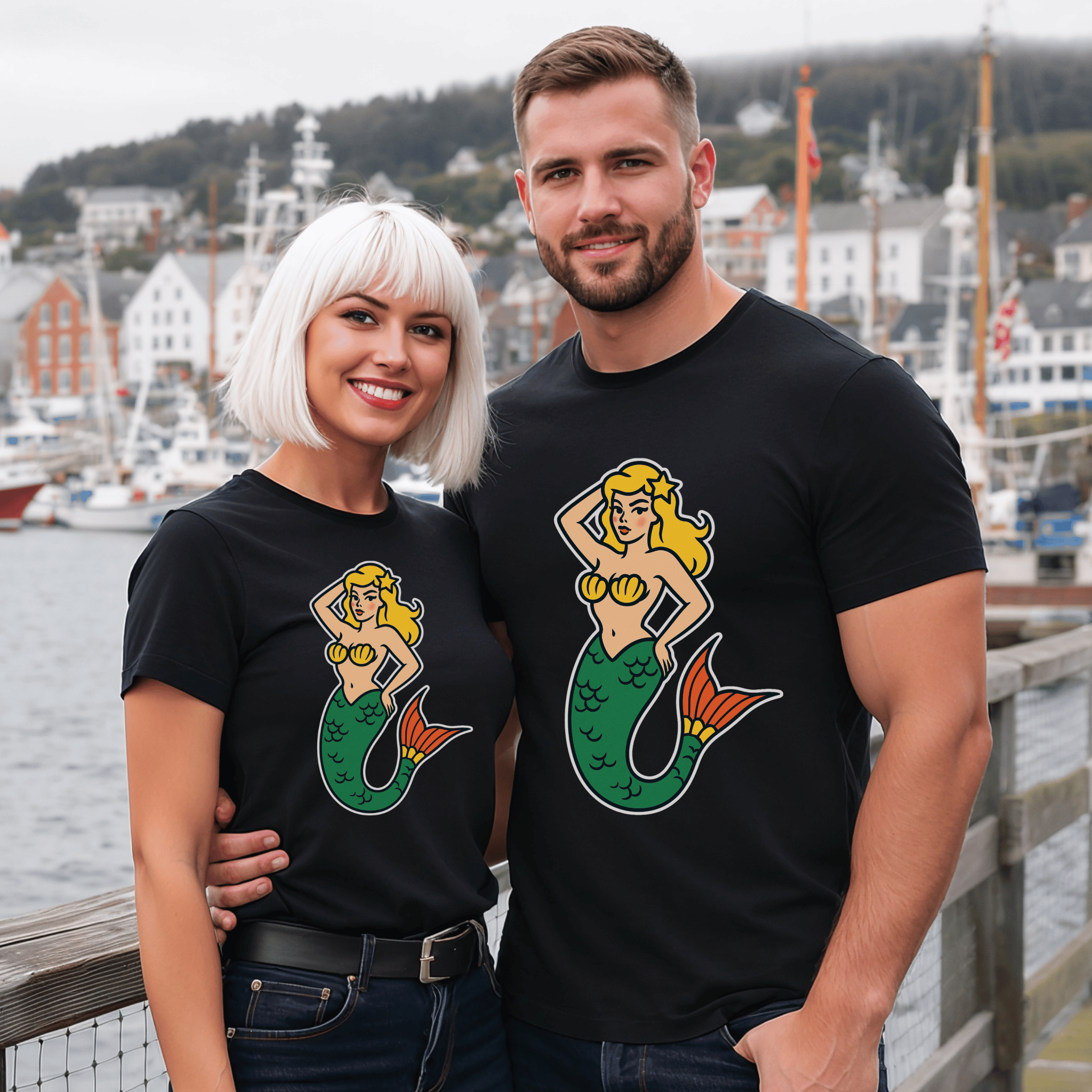 Stunning man and woman wearing matching black t-shirts with a blonde mermaid graphic in a harbor setting