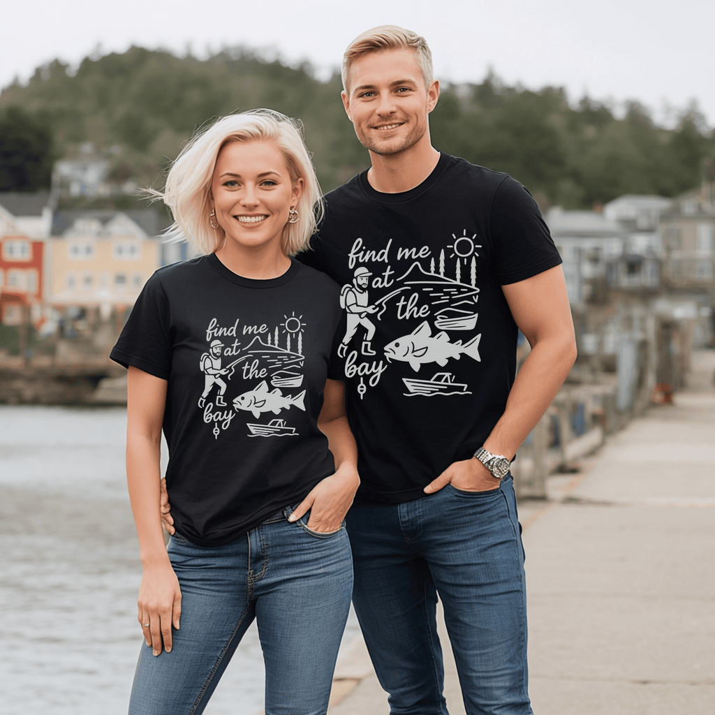 Two attractive people wearing matching black t-shirts with a graphic design of a cod, fisherman and boat and the text, "find me at the bay."