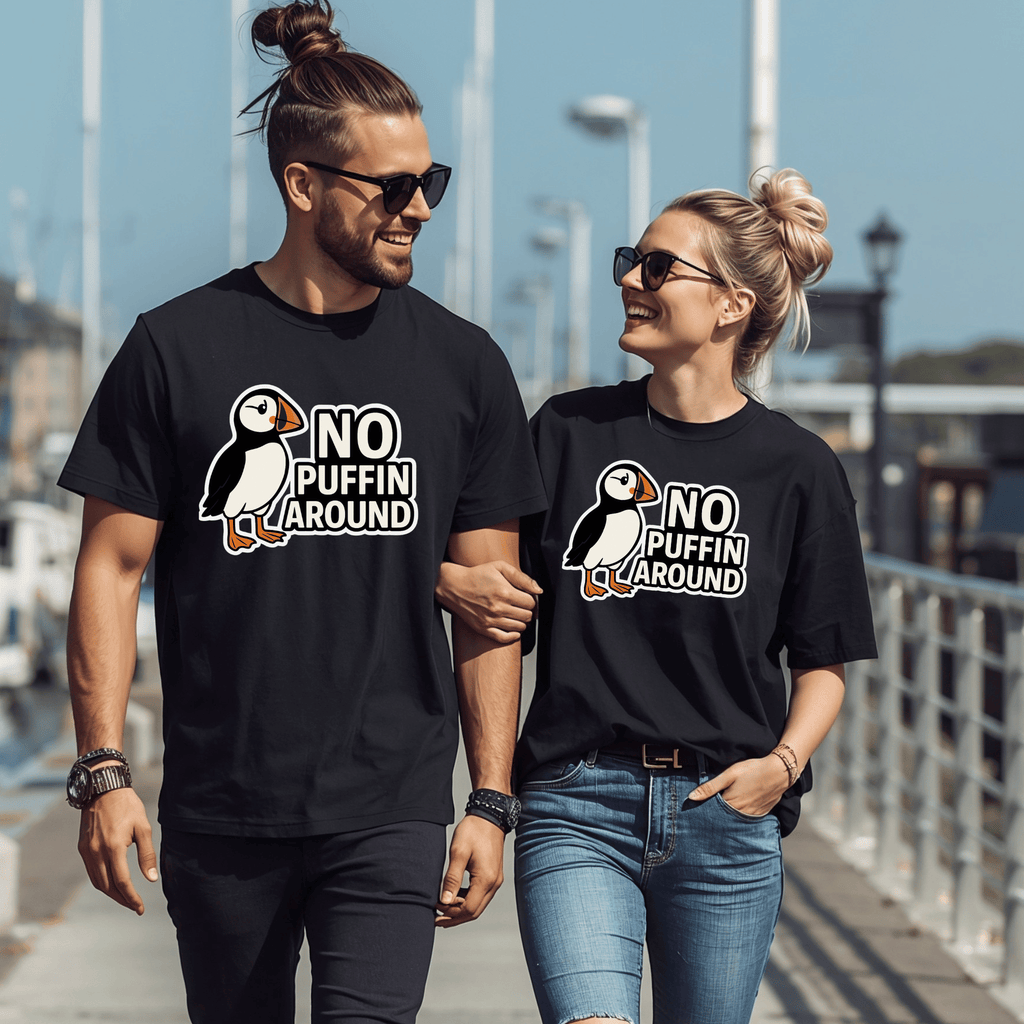 A couple walking on a harbor wearing black t-shirts that have a puffin and the text "No Puffin Around."
