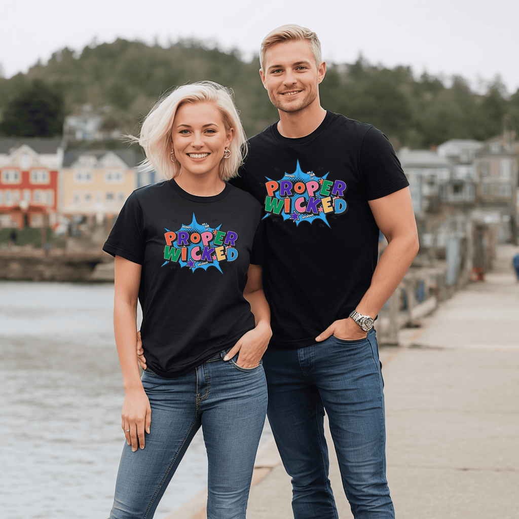 Two attractive people wearing matching black t-shirts with colorful text saying "Proper Wicked" standing by a waterfront.