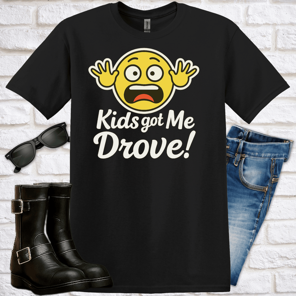 Black t-shirt with a hysterical yellow emoji and text 'Kids got Me Drove!' on a white brick background, with boots. glasses and jeans for scale.