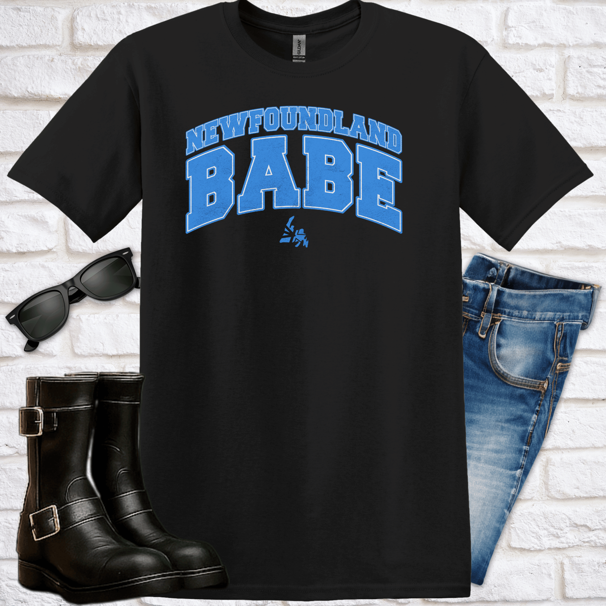 Black t-shirt with 'Newfoundland Babe' text, sunglasses, boots, and jeans on a white brick background