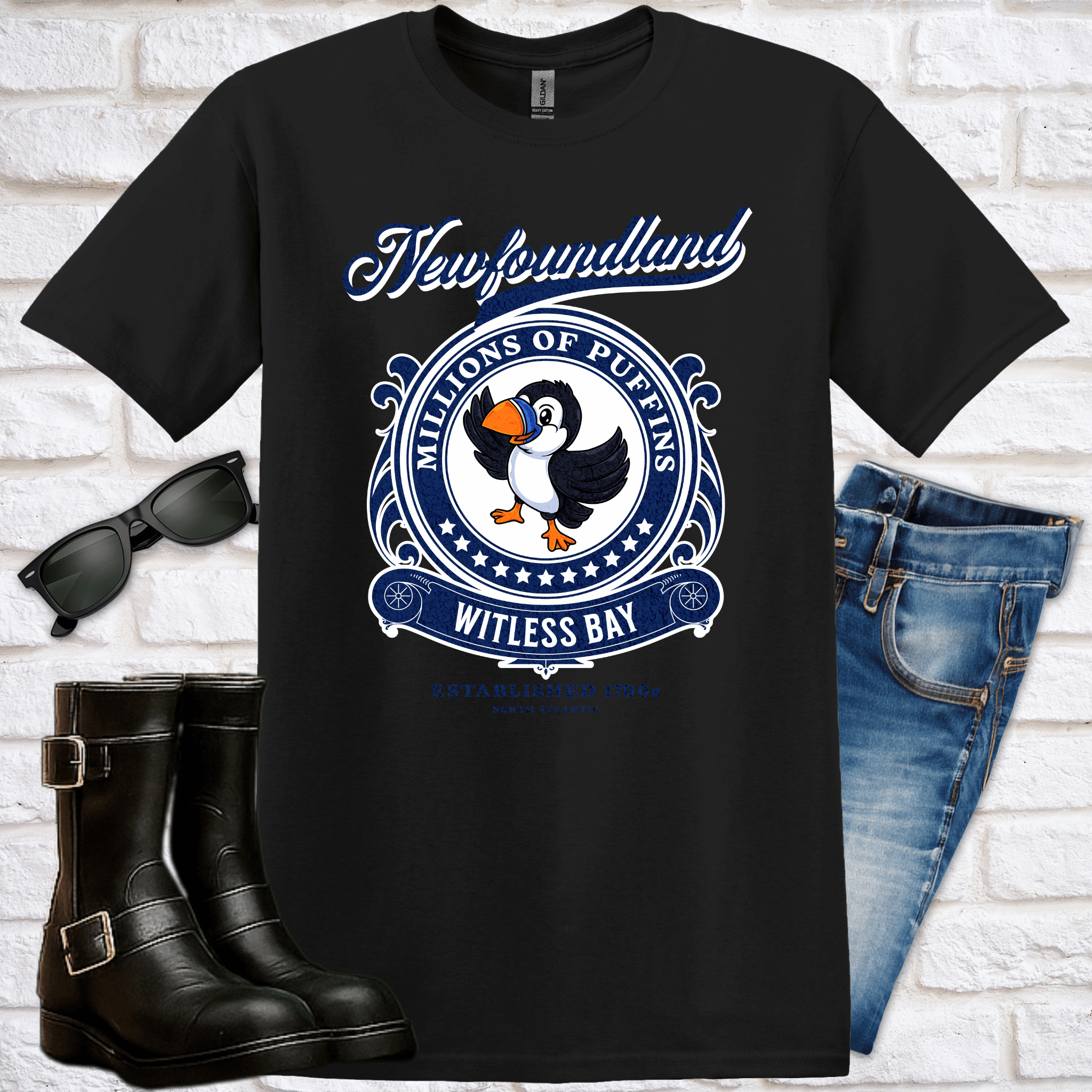Black t-shirt with a puffin design and text of "Newfoundland, Millions of Puffins, Witless Bay", sunglasses, boots, and jeans on a white brick background