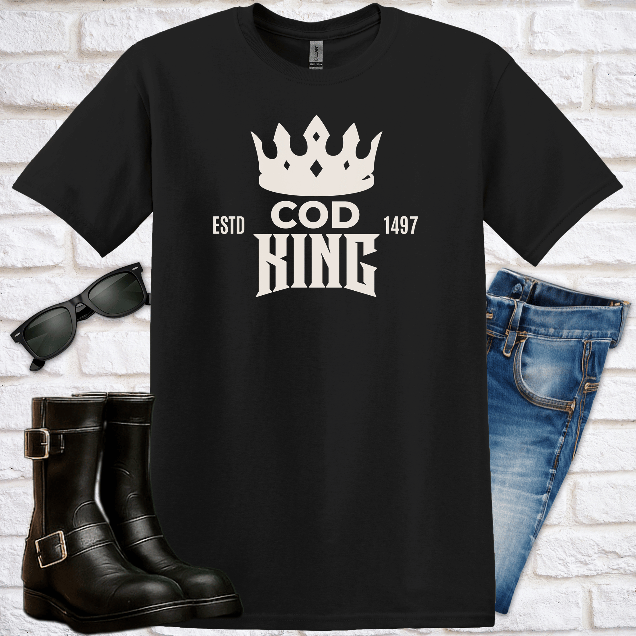 Black t-shirt with 'COD KING' design, sunglasses, boots, and jeans on a white brick background