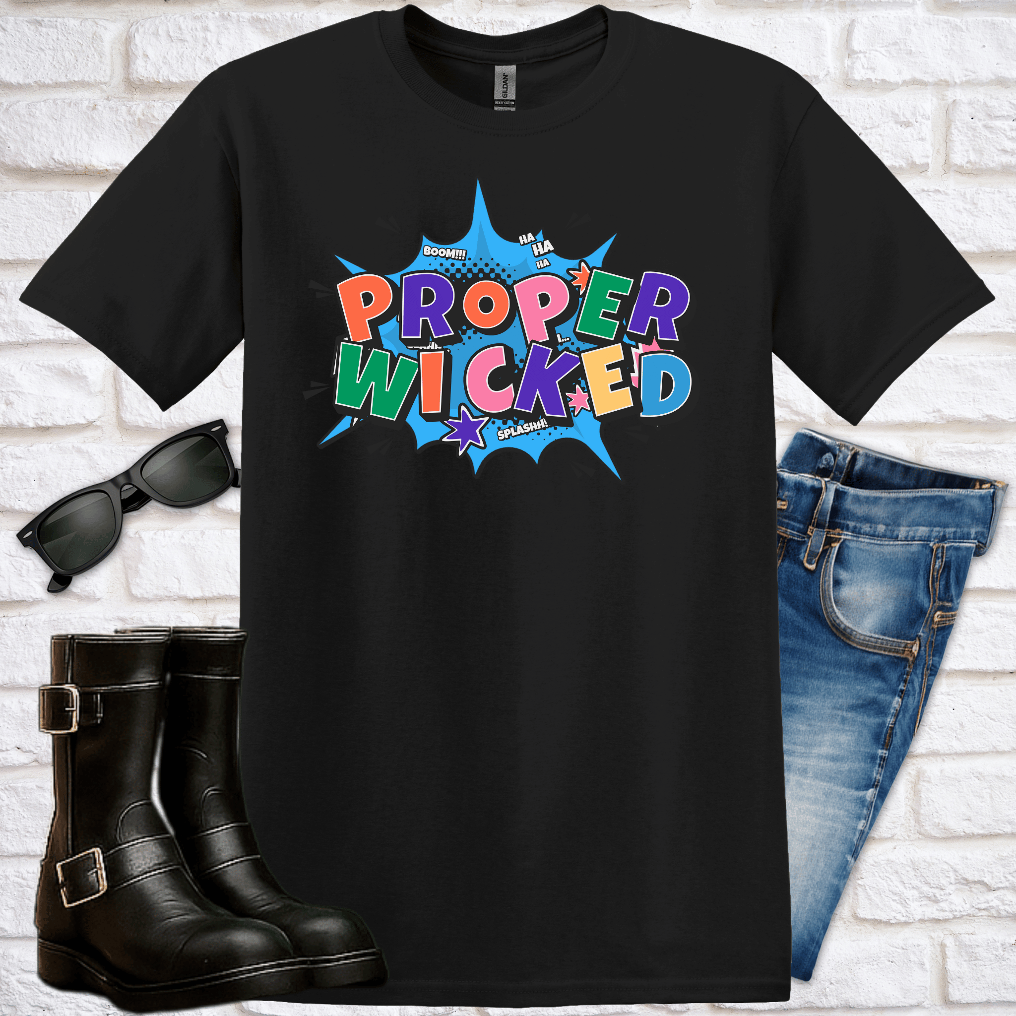 Black t-shirt with colorful comic-style 'Proper Wicked' design, sunglasses, black boots, and blue jeans on a white brick background.