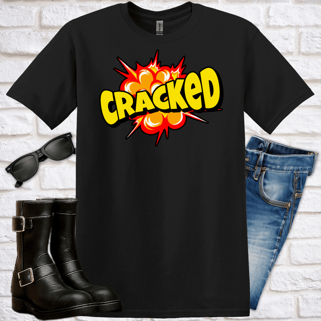 Black t-shirt with 'CRACKED' explosion graphic design, sunglasses, and jeans on a white brick background