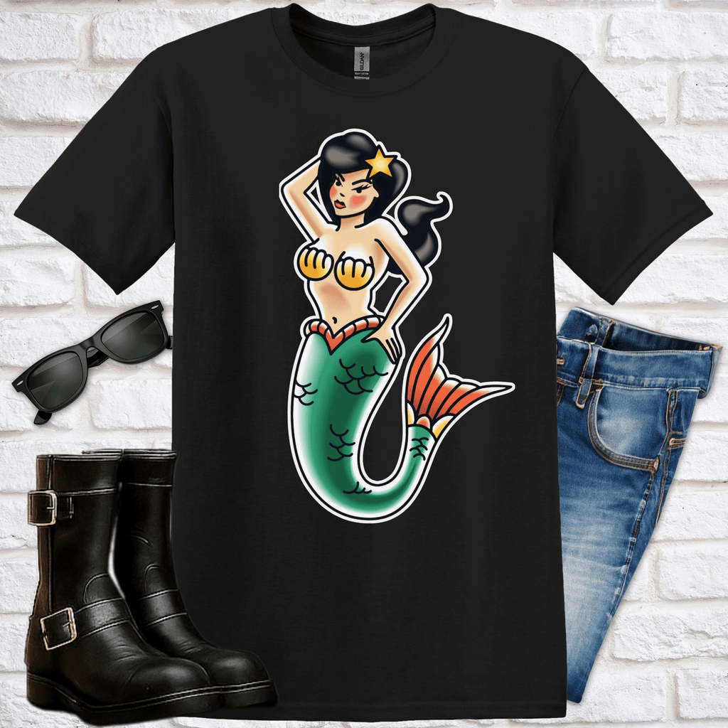 Black t-shirt with a brunette-haired mermaid graphic, sunglasses, boots, and jeans on a white brick background