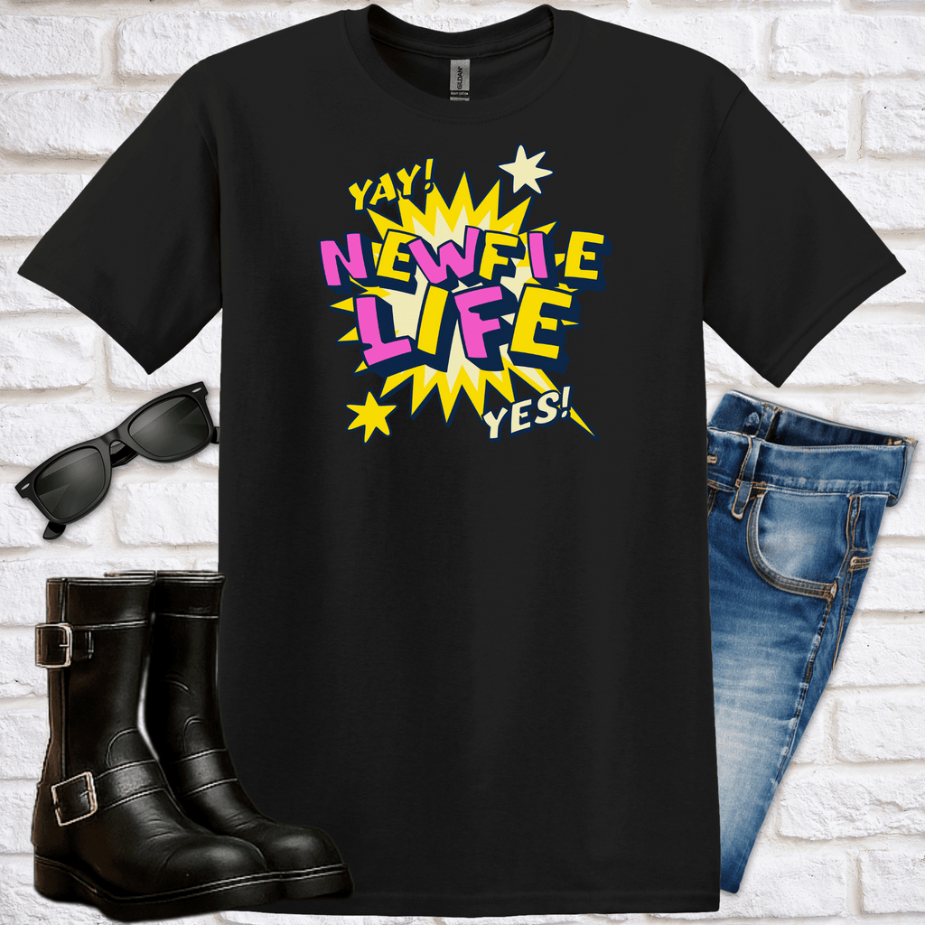Black t-shirt with colorful text design saying Newfie Life, sunglasses, boots, and jeans on a white brick background