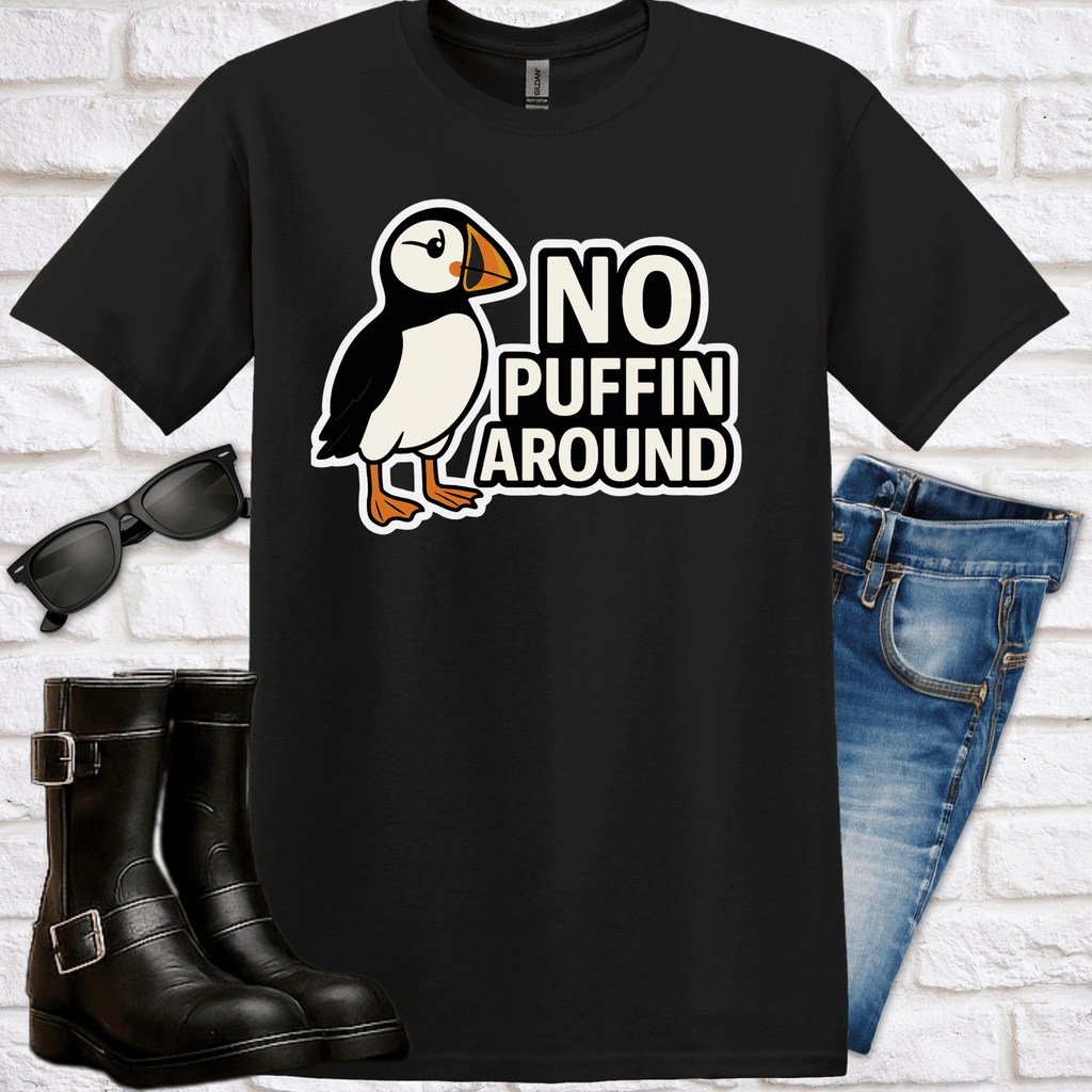 Black t-shirt with a puffin graphic and 'No Puffin Around' text, displayed with sunglasses, boots, and jeans on a white brick background.